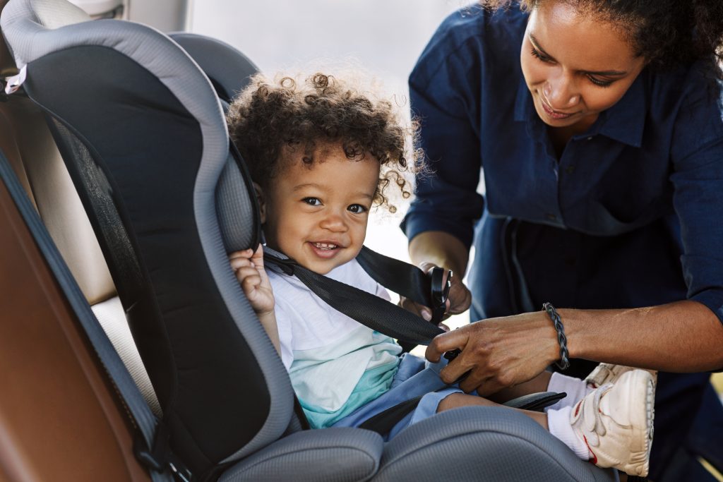 Boy looking at camera while mother buckles him in a car seat